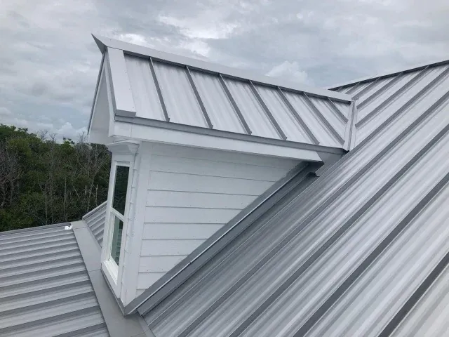 Close-up of a finished standing seam metal roof at a dormer, showing the valley flashing and ridge cap detail